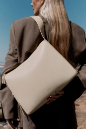 Model with long blonde hair wearing a brown blazer carrying a large cream leather shoulder bag against a blue sky