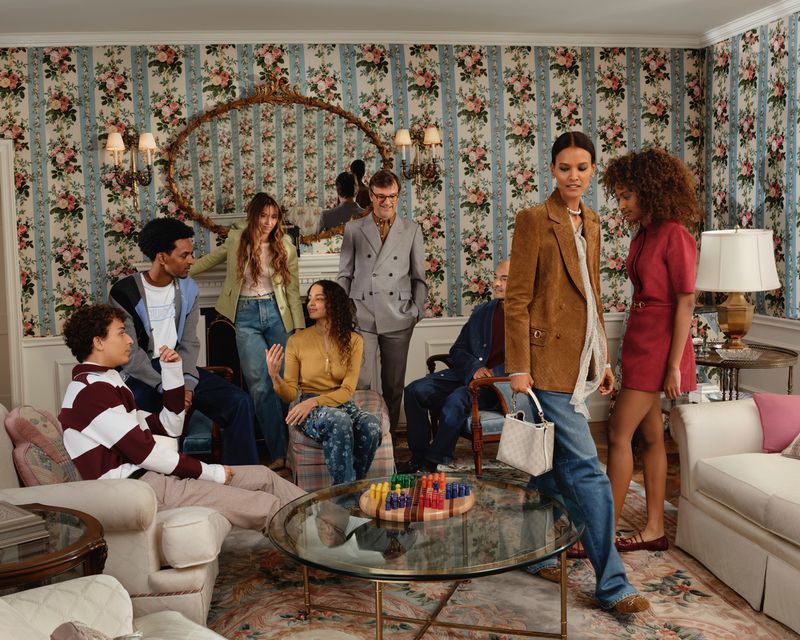 Group of diverse adults and young adults are indoors in a living room with floral wallpaper and playing a board game.