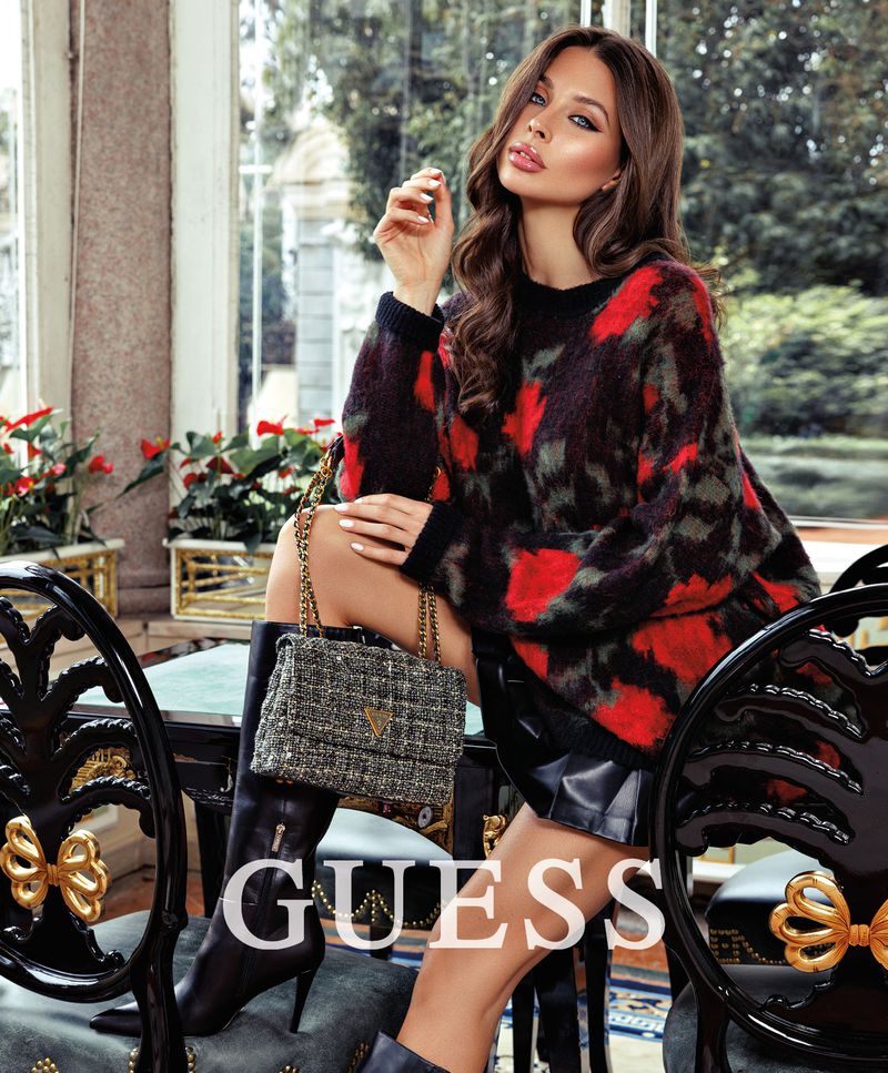 Model Francesca Valenti posing with a tweed handbag, wearing a red patterned sweater and black boots for Guess