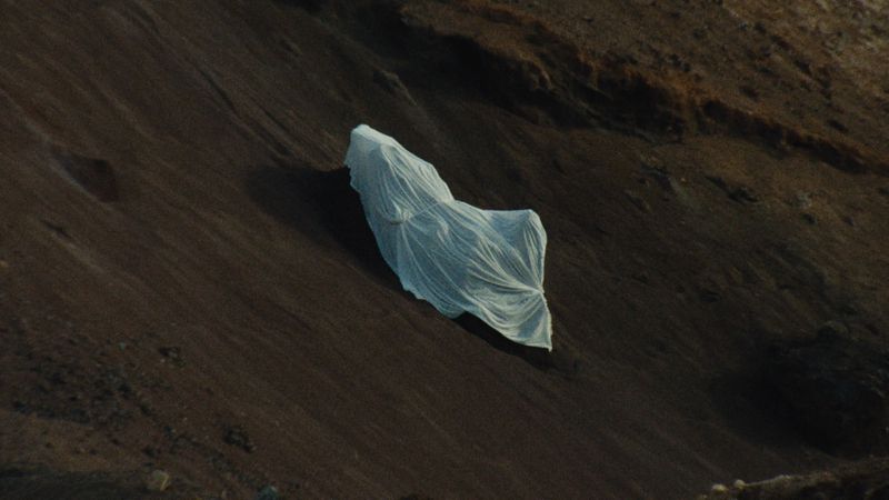 A dramatic outdoor shot featuring an object covered in white cloth, set against a brown landscape, creates a visually intriguing contrast.