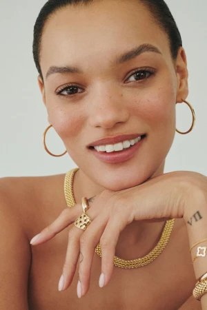 Close-up portrait of model Lameka Fox wearing gold hoop earrings and fine jewelry necklaces against a neutral background