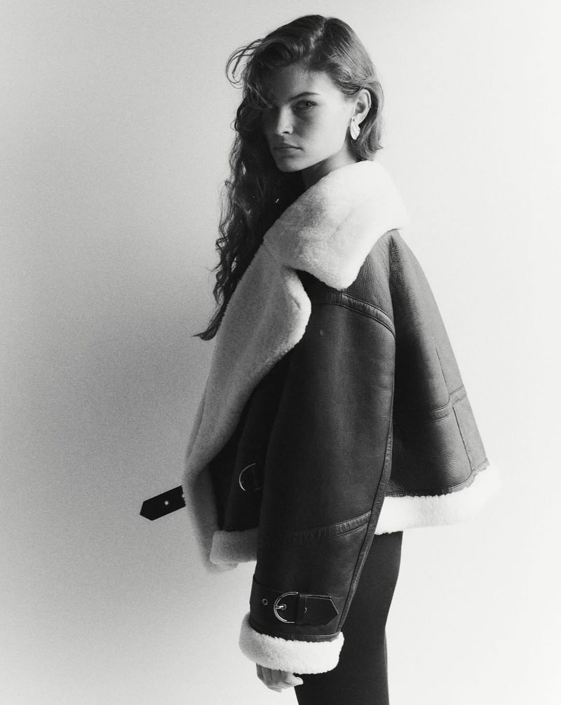 Portrait of a woman wearing a shearling-lined leather jacket against a white background in a studio setting.