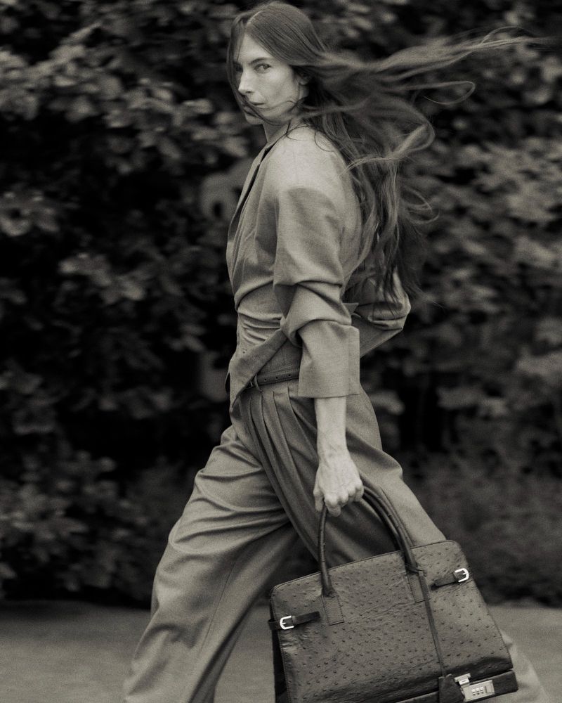Monochrome portrait of a woman in an outdoor setting, styled in a light-colored suit with a handbag, creating a blend of fashion and nature.