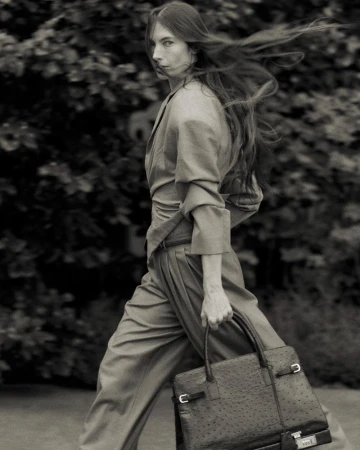 Monochrome portrait of a woman in an outdoor setting, styled in a light-colored suit with a handbag, creating a blend of fashion and nature.