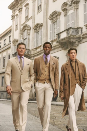 Three well-dressed men in suits walking on a city street with ornate buildings, showcasing fashion and style.