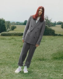 Model with long red hair wearing a grey double-breasted suit standing in an open grassy field