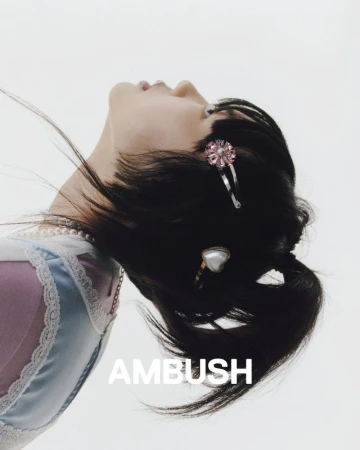 Woman with dark hair accented with hair clips, wearing a pastel-colored dress, looking up against a bright white background.