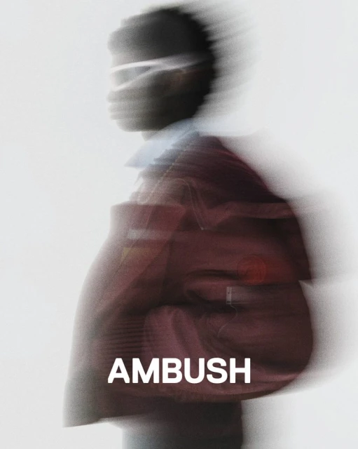 Blurred motion fashion shot featuring an adult with a maroon jacket against a bright white background with the word 'AMBUSH' in the foreground.