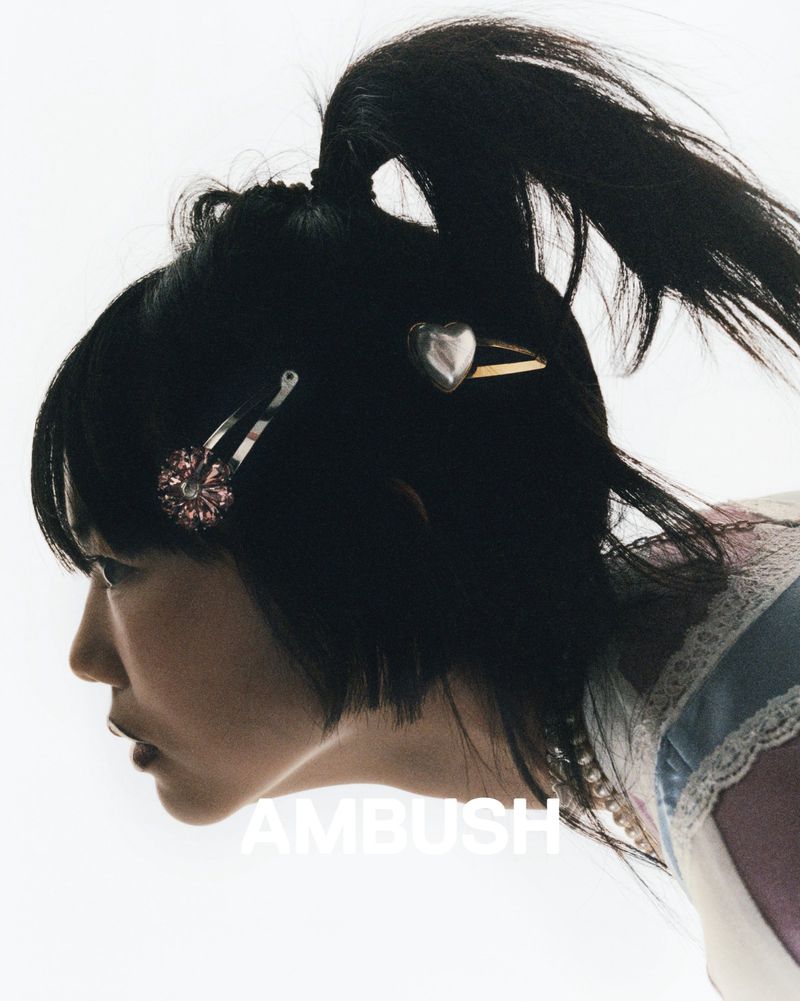 Profile of a woman with black hair styled in a high ponytail, adorned with silver heart and floral hair clips against a white backdrop.