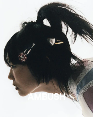 Profile of a woman with black hair styled in a high ponytail, adorned with silver heart and floral hair clips against a white backdrop.