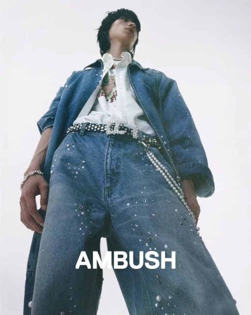 Stylish person poses in denim jacket and jeans with pearl accents against a bright background, showcasing high-fashion street style.