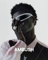 Black man wearing futuristic sunglasses and a patterned shirt with a large silver ring against a white background