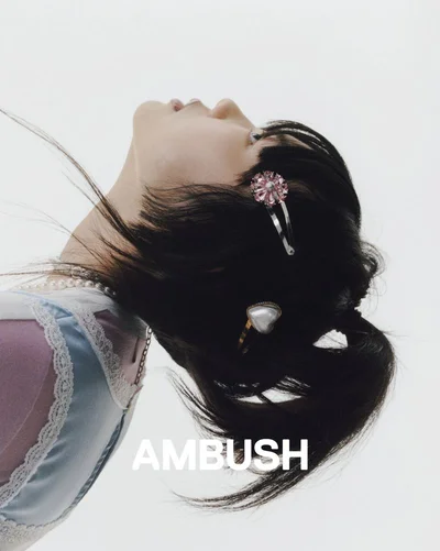 Profile view of a woman with dark hair styled with two hair clips against a plain white background for AMBUSH