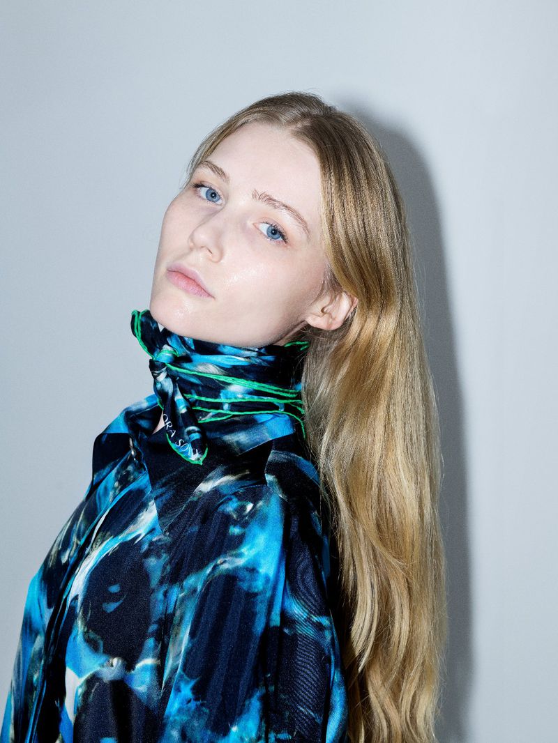 Close-up portrait of a woman with long blonde hair wearing a bright blue patterned silk scarf and matching patterned top.