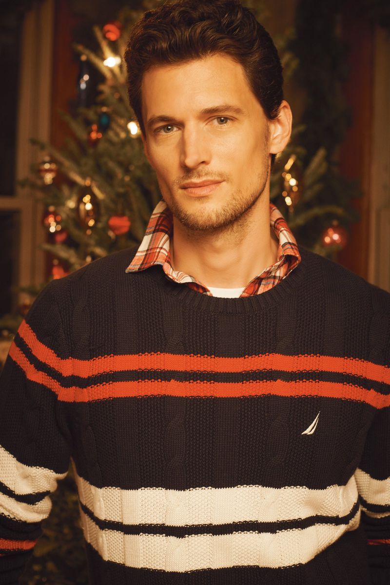 Adult male with brown hair in a striped sweater posing indoors, with a Christmas tree visible in the background.