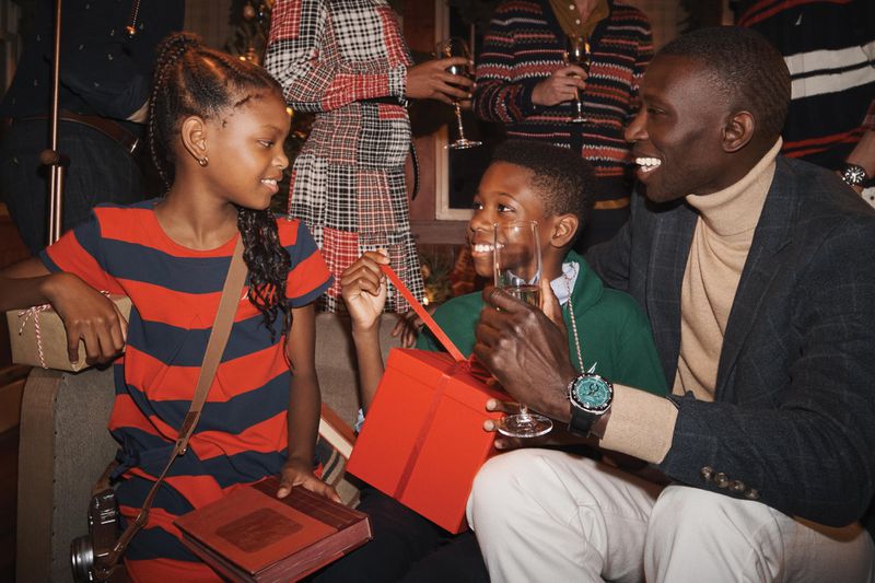 A joyous holiday gathering featuring children opening gifts, a smiling adult, and a festive backdrop with wine glasses and holiday decorations.