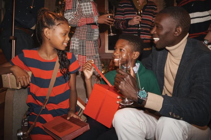 A joyous holiday gathering featuring children opening gifts, a smiling adult, and a festive backdrop with wine glasses and holiday decorations.