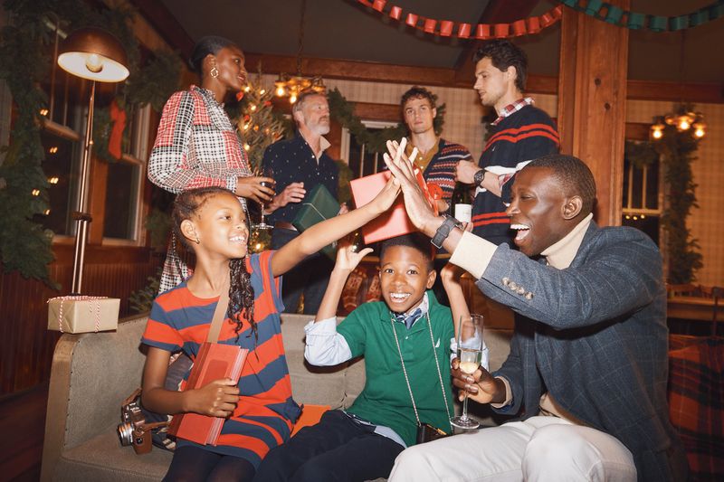 Group of diverse people celebrating a holiday indoors with a Christmas tree, gifts, champagne, and festive decorations.