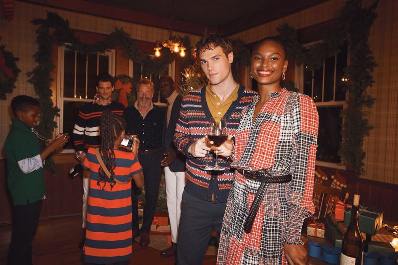 Indoor group photo features a man holding wine with a smiling woman in a plaid dress, children taking photos, and holiday decorations.