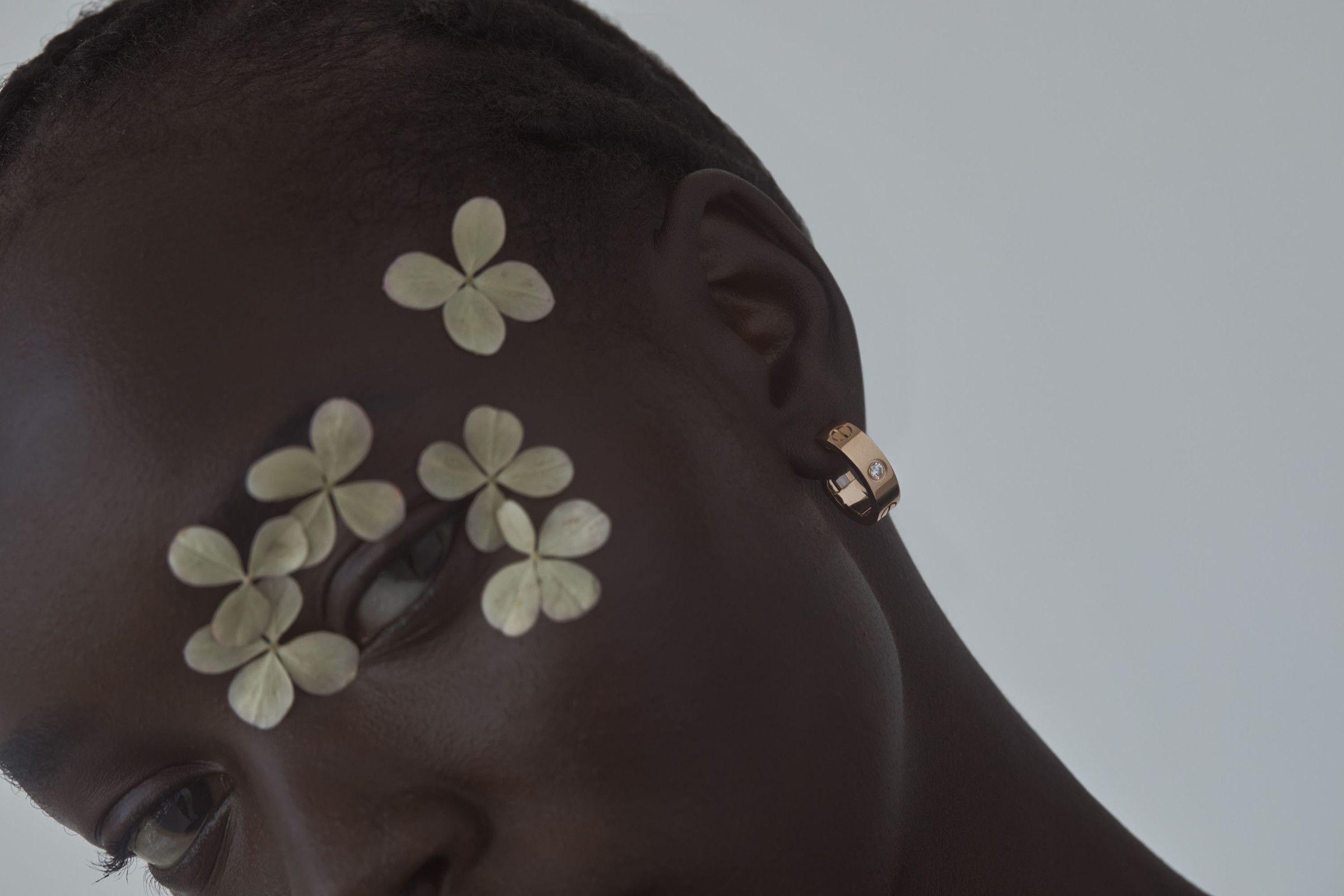 Close-up of an adult female with dark hair and skin, wearing gold hoop earrings, and adorned with white flowers on her face.