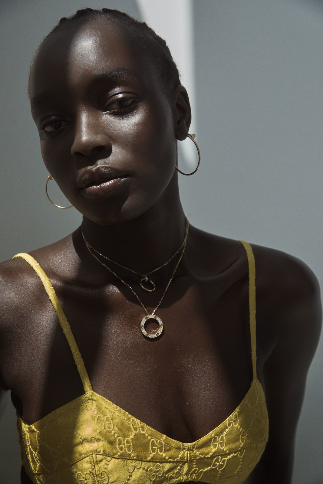 Close-up portrait of a dark-skinned adult female wearing a yellow top and jewelry, with dramatic lighting and a grey background.