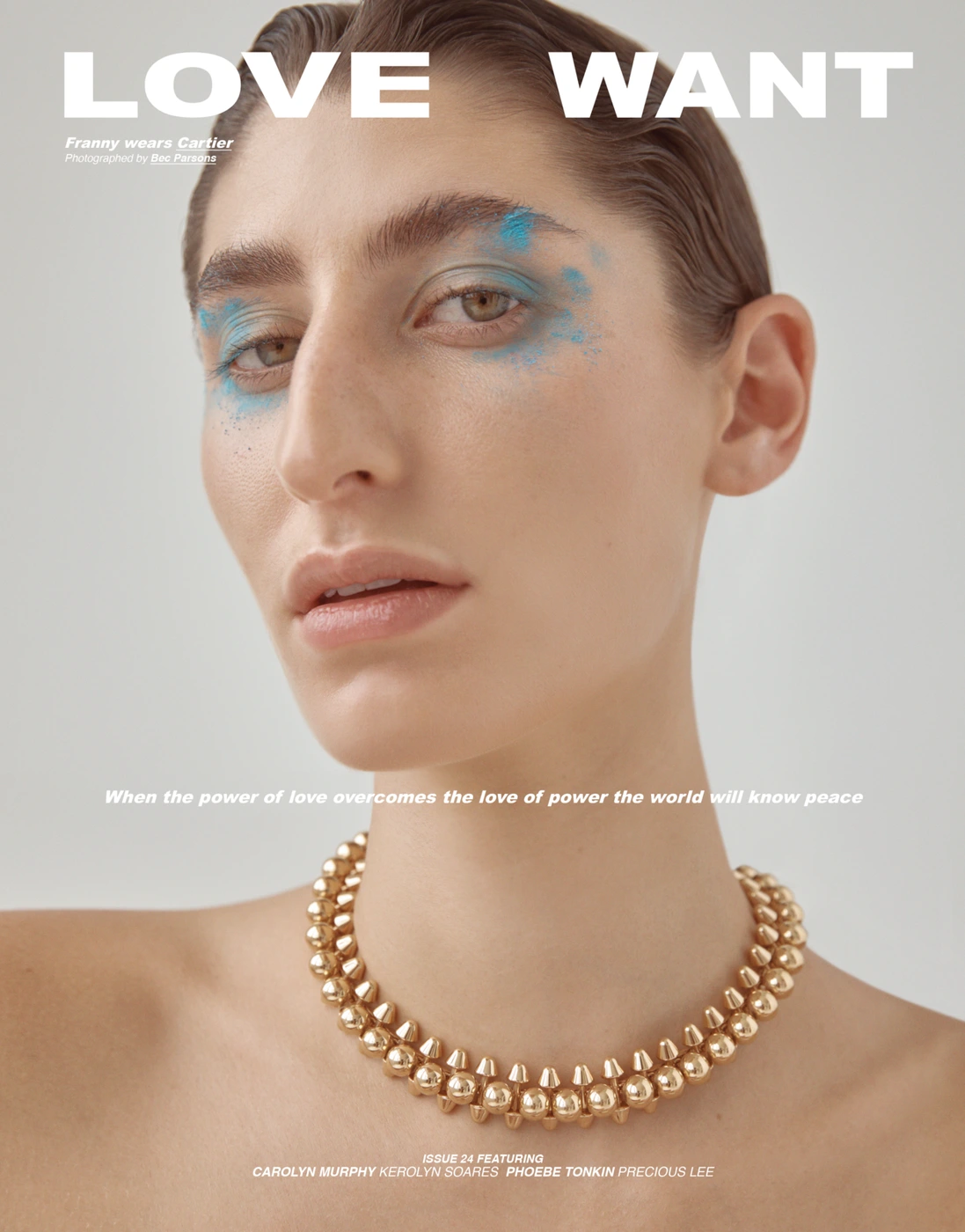 Close-up portrait of a woman wearing a heavy gold beaded necklace and blue eyeshadow against a plain light background