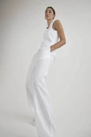 Model wearing a white sleeveless vest and wide-leg trousers posing against a clean white background
