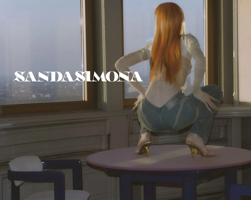 A slender, red-haired woman poses in jeans and a top in an indoor setting, leaning on a table near a window with city views.