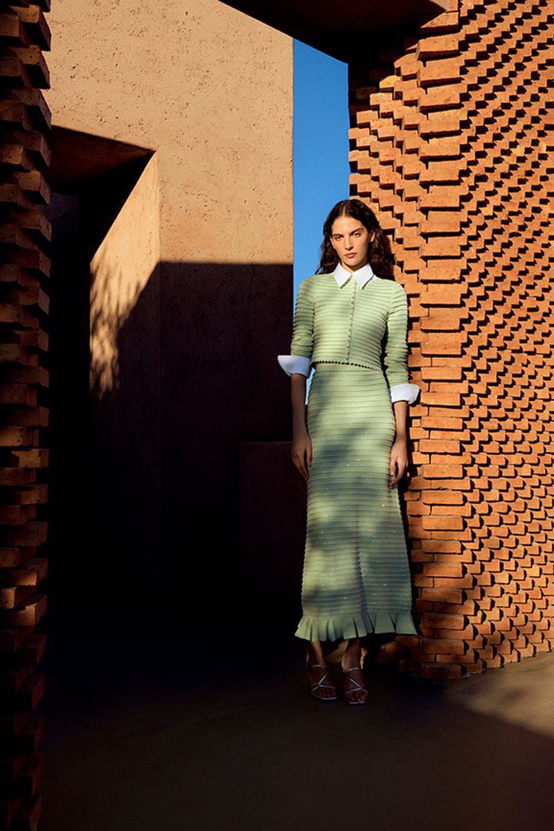 Fashion portrait of an adult woman in a light green dress posing in a brick structure with open blue sky visible behind her.