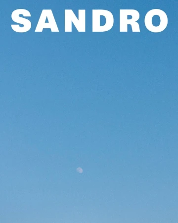Clear blue sky with large white brand text at the top and a small crescent moon visible below for Sandro S/S 25