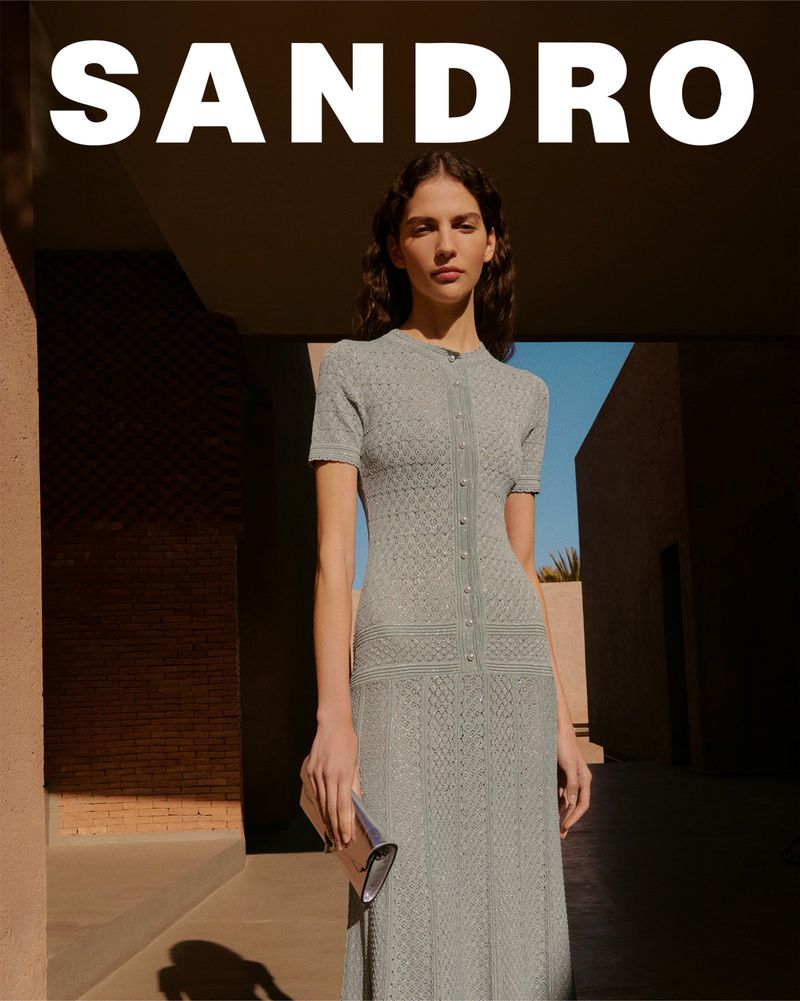 Fashion shot: Adult female poses in a knitted dress with a clutch against an urban backdrop, showcasing a blend of style and setting.