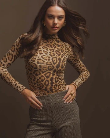 Woman in a leopard print top and patterned trousers posing against a dark background for the TALCO FW24/25 campaign.