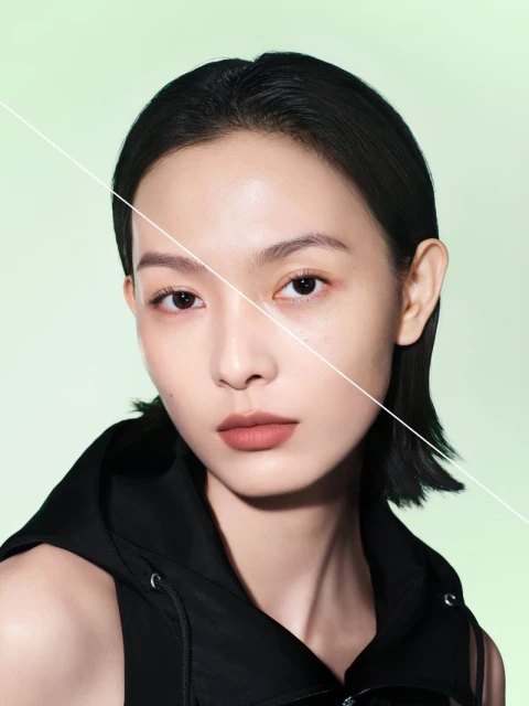 Close-up portrait of an Asian woman in a black hooded top against a light green background, divided diagonally by a white line.