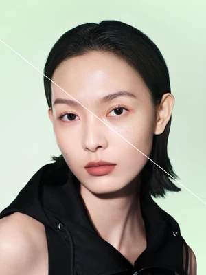 Close-up beauty portrait of an East Asian woman with dark hair wearing a black top against a light green background with a diagonal white line