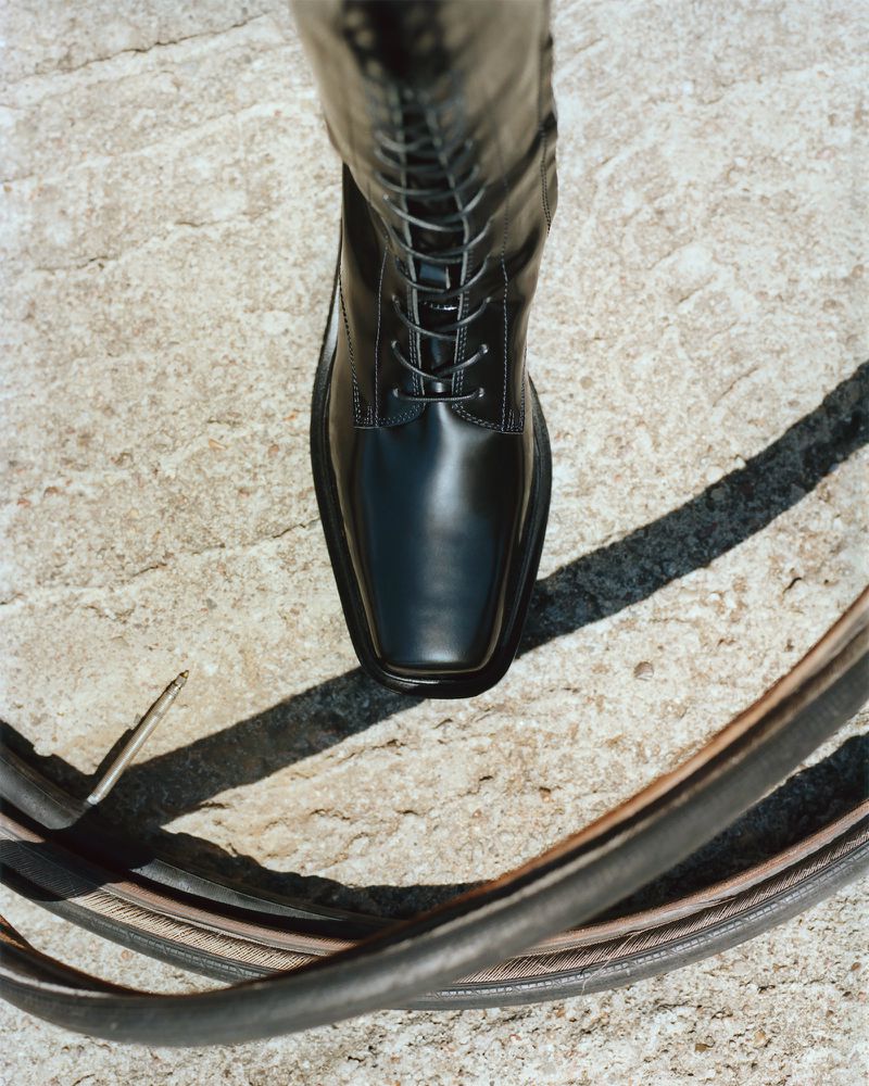 Top-down shot of a black leather boot with laces on concrete, with a section of black bicycle tire visible in the foreground.