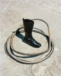 Black leather lace-up combat boot placed inside coiled strips on a textured stone ground.