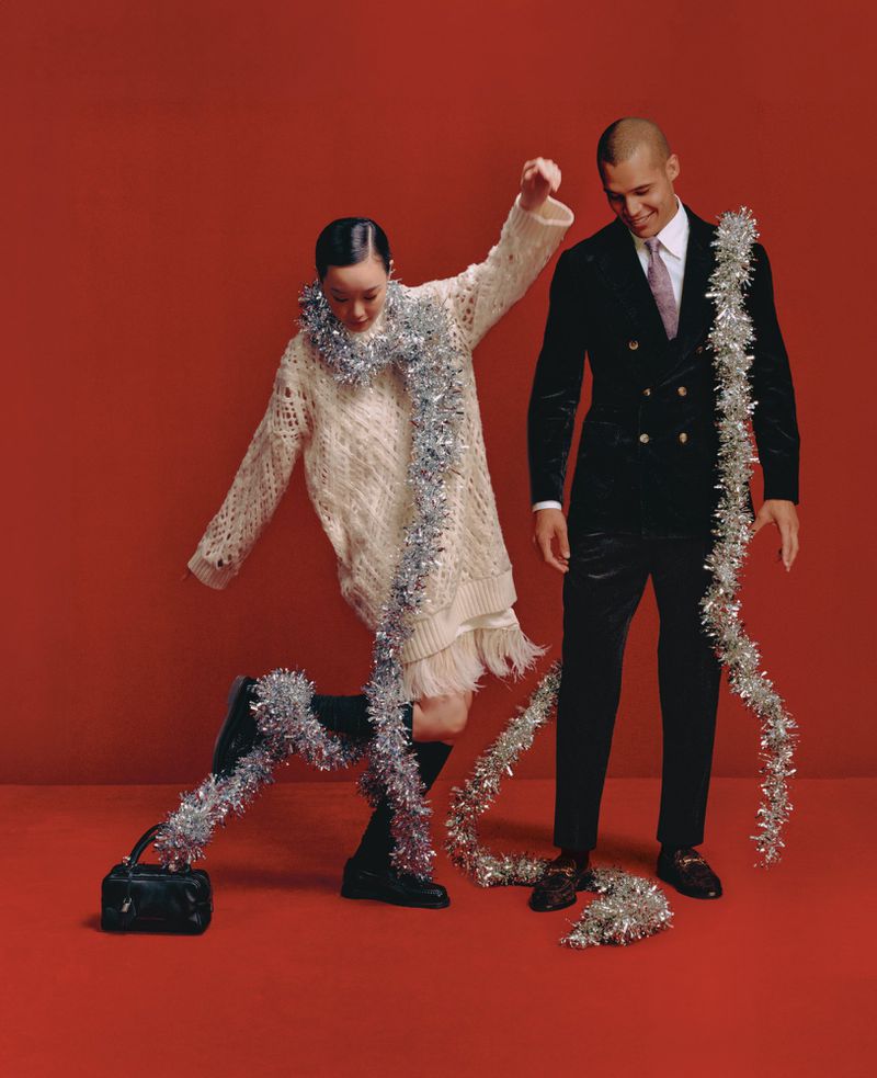 A fashionable couple poses in a photo studio against a red backdrop, adorned with silver tinsel, displaying elegance and festive charm.