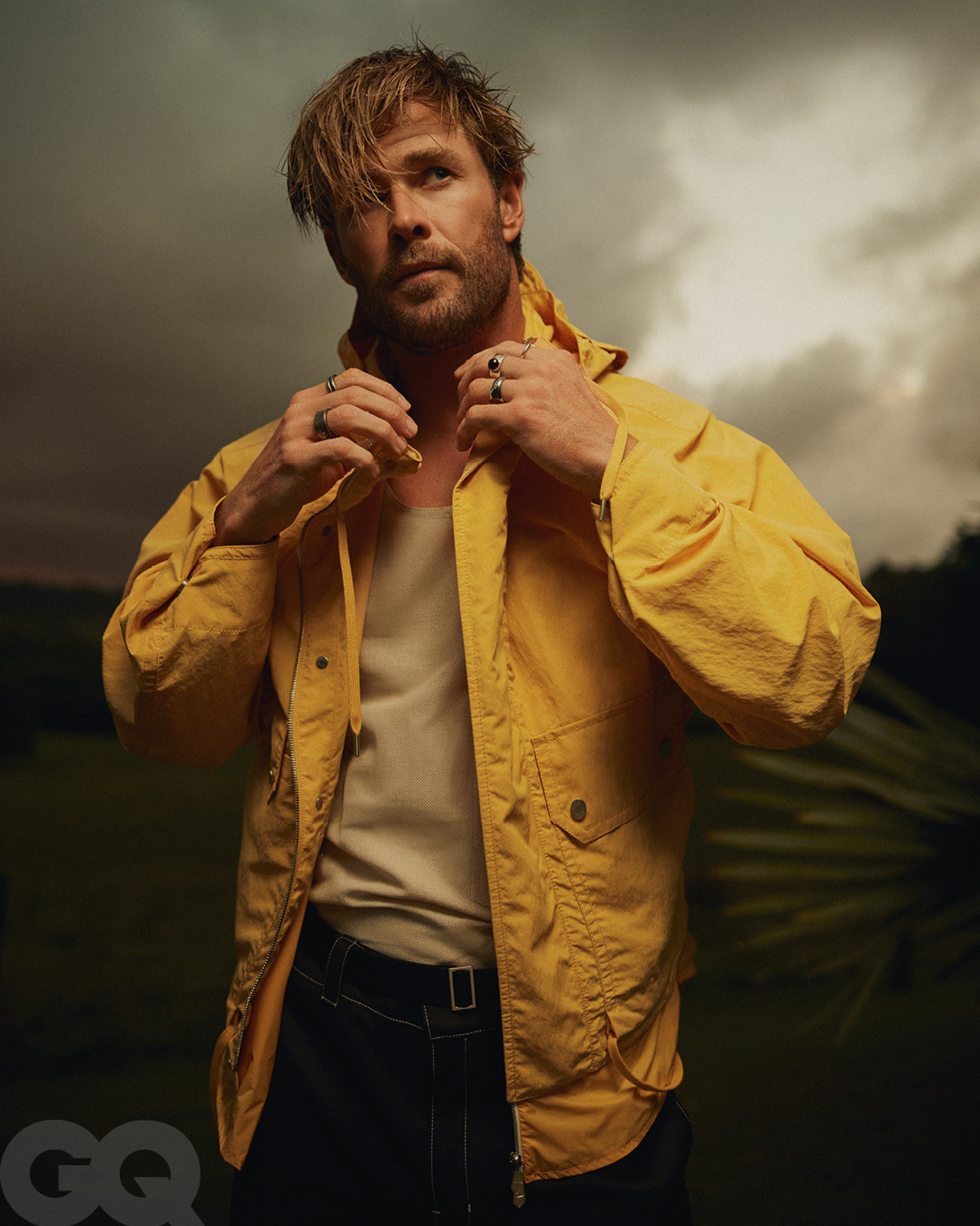 Chris Hemsworth in a yellow hooded jacket and white tank top against an overcast sky for British GQ