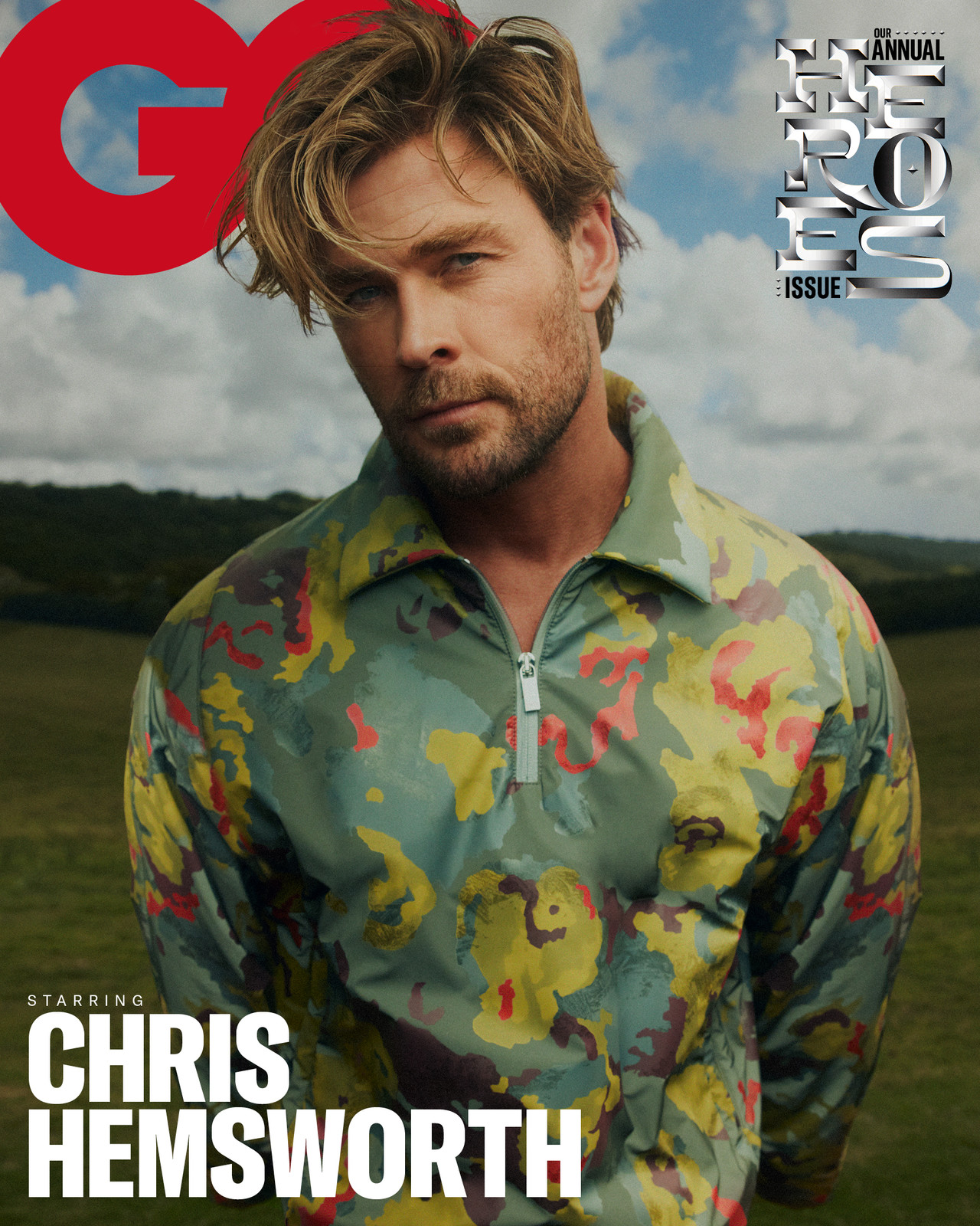 Chris Hemsworth on GQ cover, wearing a colorful floral-patterned jacket. He is posing in front of a green landscape and blue sky.