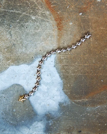 Close-up of a gold star-shaped link bracelet on a grunge background featuring a weathered surface with scratches and discoloration.