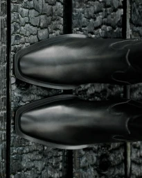 Top-down view of black leather cowboy boots resting on a dark charred wooden surface.