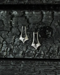 Silver earrings resting on a dark charred wooden surface with deep cracks and granular texture.