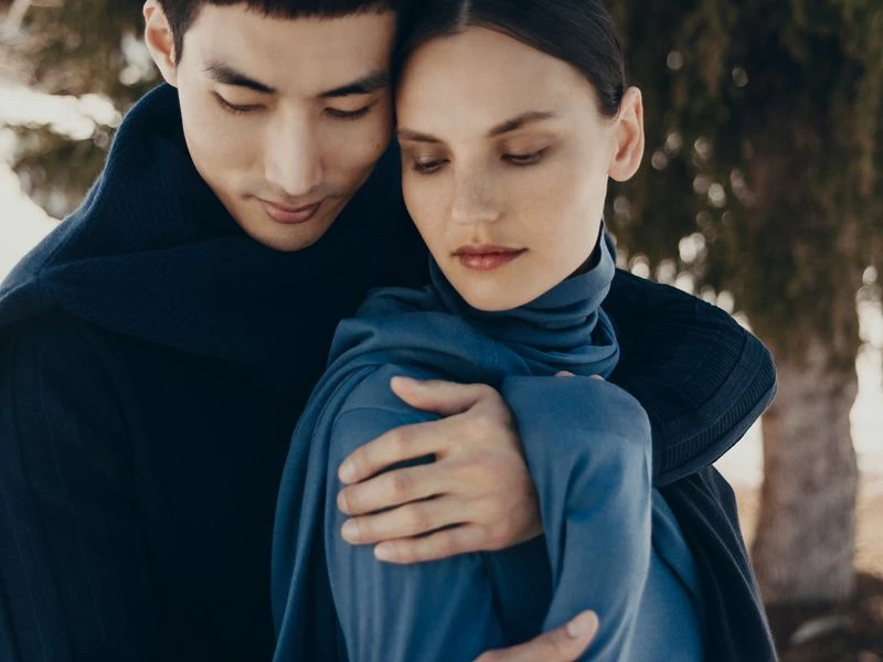 Intimate portrait of a couple in a close embrace outdoors, dressed in matching blue tones, set against a blurred natural background of trees.