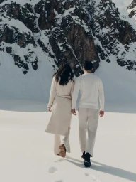 Rear view of a couple walking away on a snowy expanse toward a rocky mountain under natural daylight