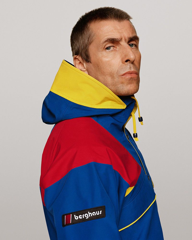 Close-up profile portrait of a male adult wearing a blue, yellow, and red hooded jacket in a photo studio against a neutral background.