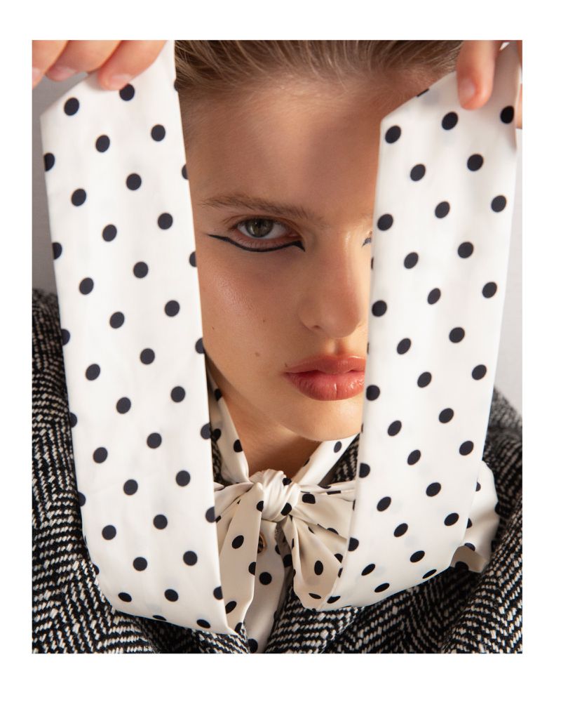 Close-up of a woman with dramatic eyeliner and a polka dot scarf tied around her neck, partially obscuring her face.