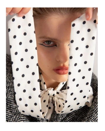 Close-up of a woman with dramatic eyeliner and a polka dot scarf tied around her neck, partially obscuring her face.