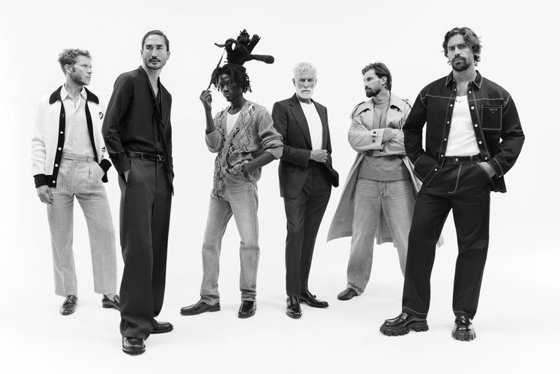 Group of six diverse adult male fashion models in casual and semi-formal wear posing against a white backdrop in a studio.