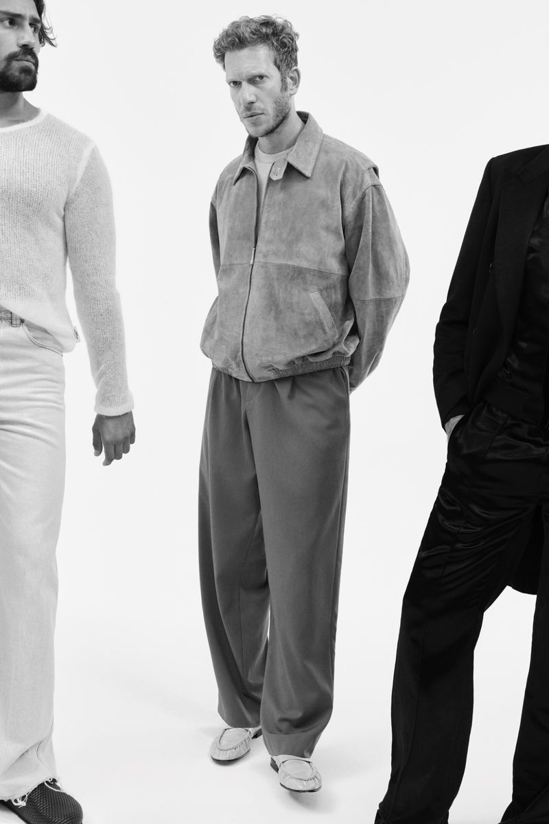 Three adult male fashion models pose in a black and white studio shot, wearing modern casual outfits against a bright white backdrop.
