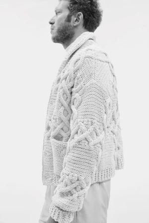 Monochrome portrait of a man in a cable knit cardigan against a light backdrop, showcasing fashion and texture. Profile view.